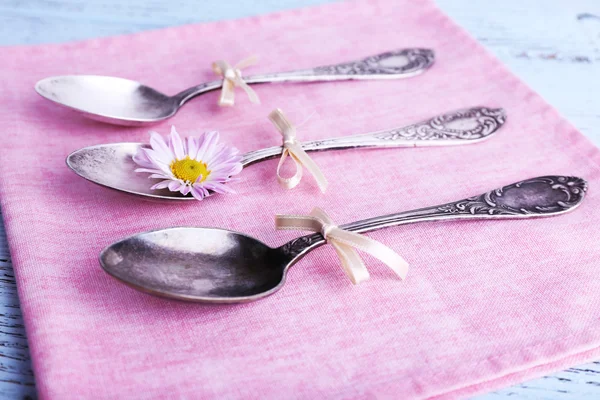 Metal spoons on pink napkin on wooden background — Stock Photo, Image