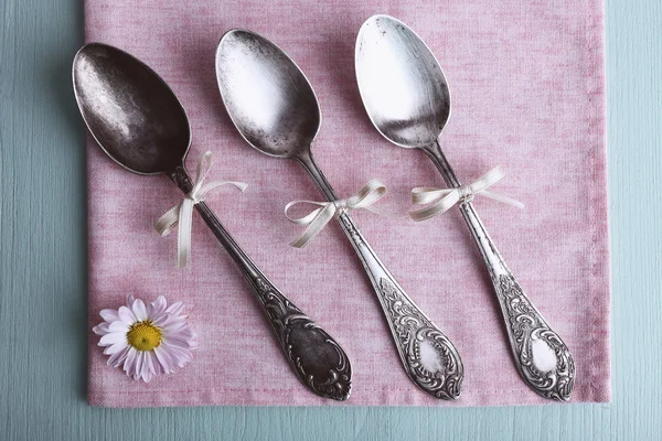 Metal spoons on pink napkin on light blue wooden background — Stock Photo, Image