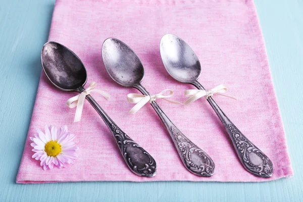 Metal spoons on pink napkin on light blue wooden background — Stock Photo, Image