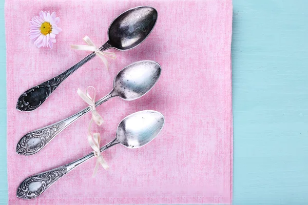 Metal spoons on pink napkin on light blue wooden background — Stock Photo, Image