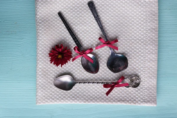 Metal spoons and dark red flower on napkin on light blue wooden background — Stock Photo, Image