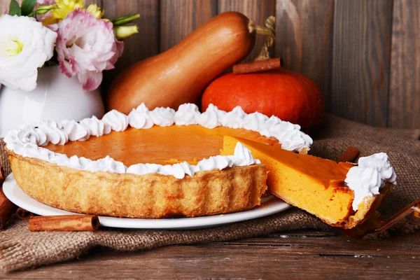 Composition of homemade pumpkin pie on plate and fresh pumpkins on wooden background — Stock Photo, Image