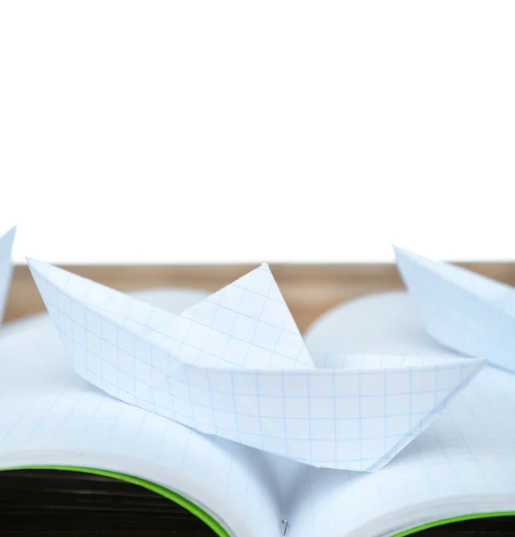 Origami boat on notebook on wooden table, on white background — Stock Photo, Image