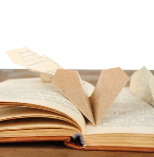 Origami airplanes on old book, on wooden table, on white background — Stock Photo, Image