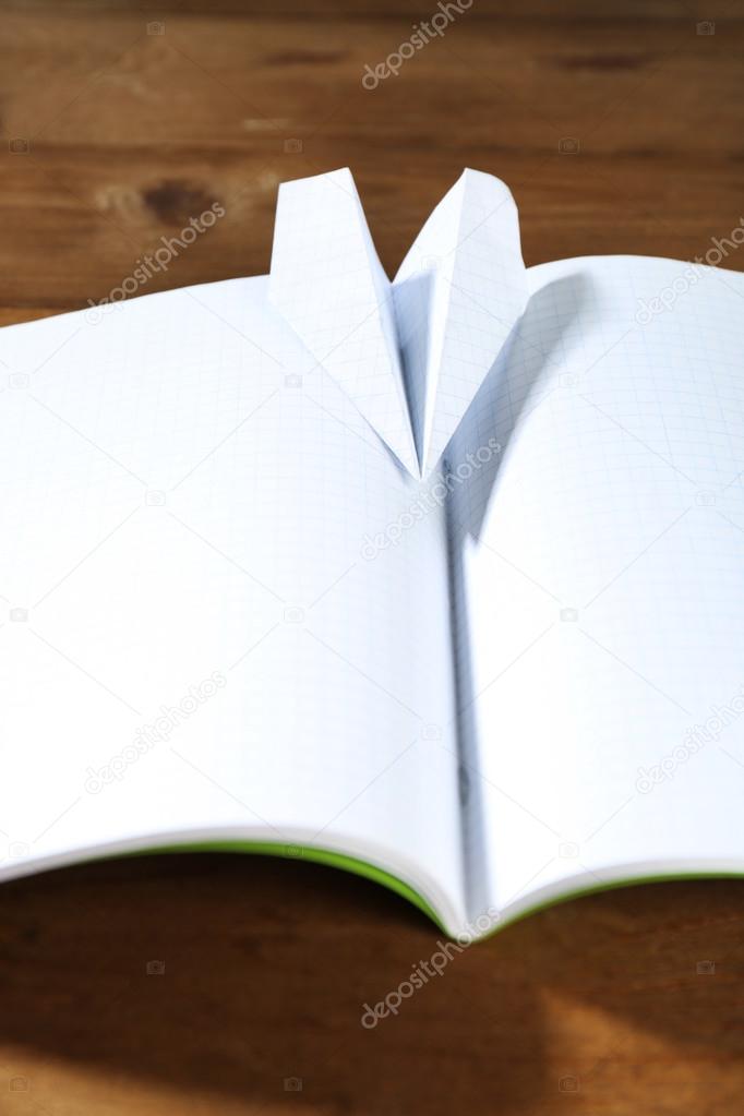 Origami airplane on notebook, on wooden table