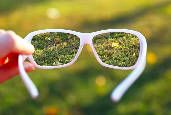Vision concept. Glasses in hand on green grass background — Stock Photo, Image