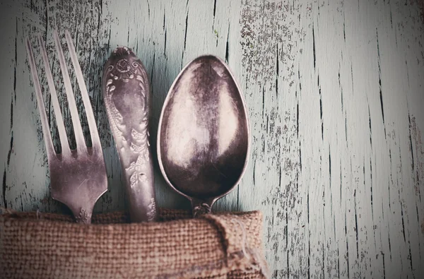 Old tableware wrapped in sackcloth napkin on wooden background — Stock Photo, Image