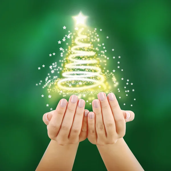 クリスマスのコンセプトです。お祭りの光沢のある背景の図形のモミの木にライトが付いて女性の手 — ストック写真
