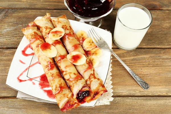 Teller mit leckeren Pfannkuchen mit Beerenmarmelade und Glas Milch auf hölzernem Hintergrund — Stockfoto