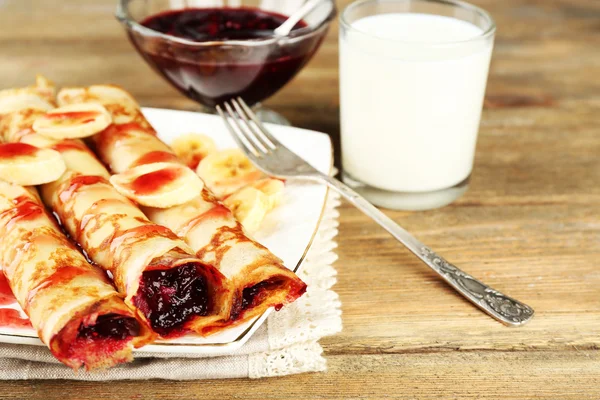 Piatto di deliziose frittelle con marmellata di bacche e bicchiere di latte su sfondo di legno — Foto Stock