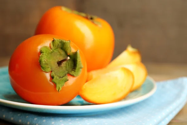 木製の背景」のプレートに熟した柿 — ストック写真