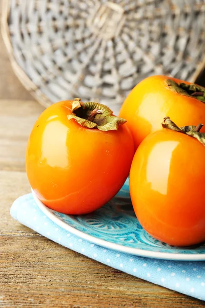 Ripe persimmons on plate, on wooden background — Stock Photo, Image