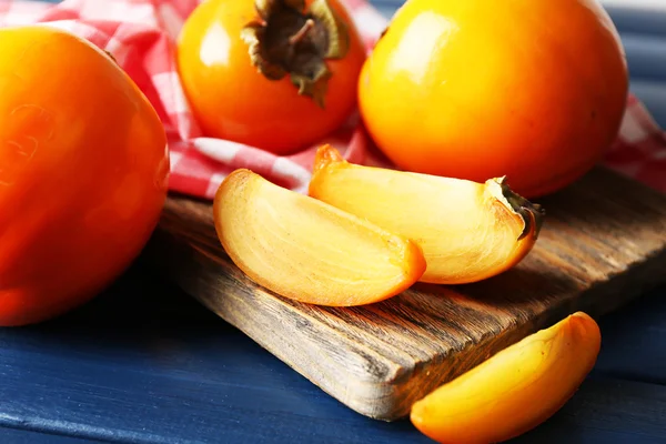 Persimmons mûrs sur planche à découper, sur fond de bois couleur — Photo