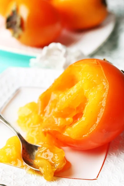 Ripe persimmons on plate, on wooden background — Stock Photo, Image