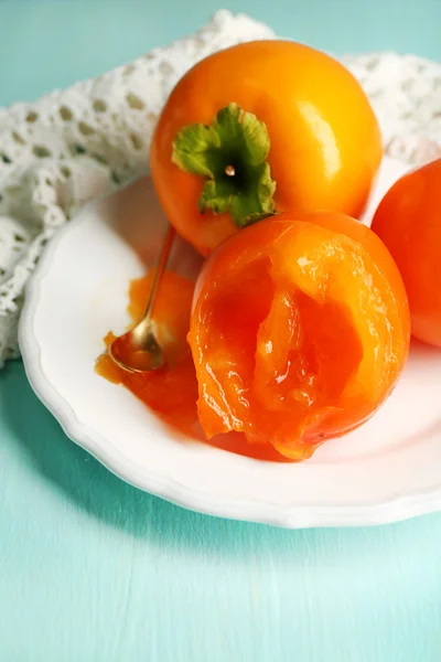 Ripe persimmons on plate, on wooden background — Stock Photo, Image