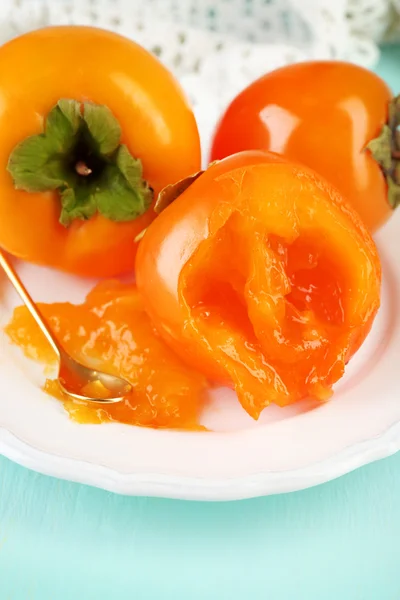 Ripe persimmons on plate, on wooden background — Stock Photo, Image