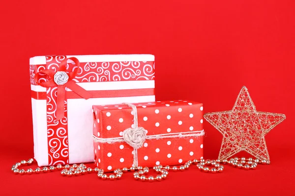 Szép fényes ajándékok és karácsonyi dekoráció, piros háttér — Stock Fotó
