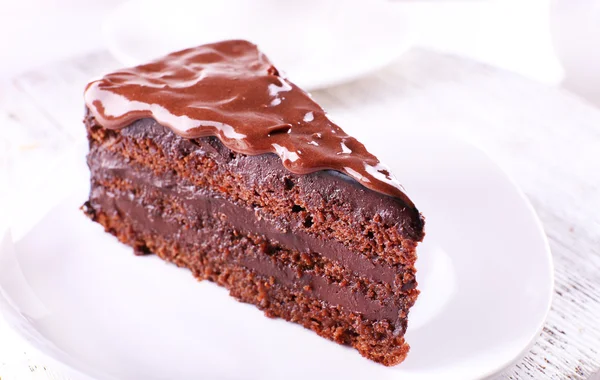 Köstlicher Schokoladenkuchen auf Teller auf Tisch vor hellem Hintergrund — Stockfoto