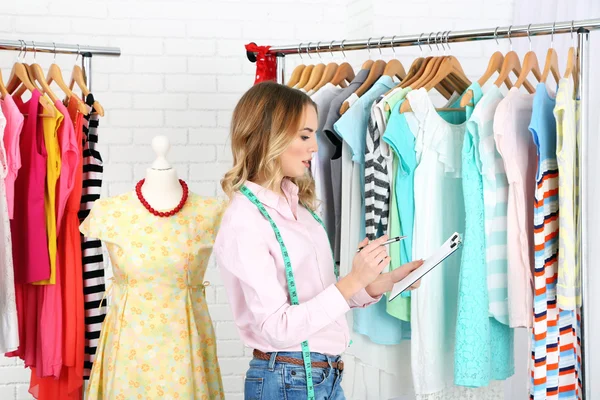 Schöne junge Stylistin in der Nähe von Gestell mit Kleiderbügeln — Stockfoto