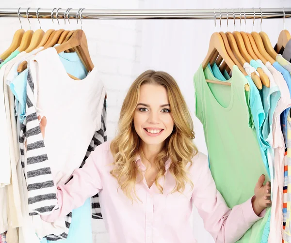 Beautiful young woman near rack with hangers — Stock Photo, Image