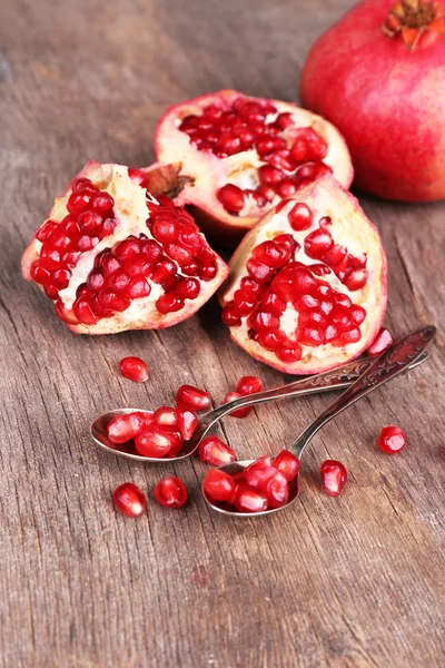 Juicy ripe pomegranates seeds in spoons, on old wooden table — Stock Photo, Image