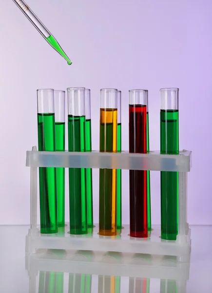 Pipetteer met daling van kleur vloeistof over container buizen op lichte achtergrond — Stockfoto