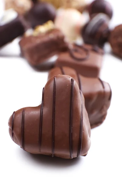 Gruppe köstlicher Bonbons mit Schokoladenherz im Vordergrund auf weißem Hintergrund — Stockfoto