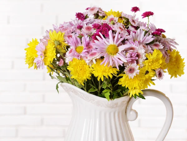 Beautiful flowers in pitcher on table on light background — Stock Photo, Image