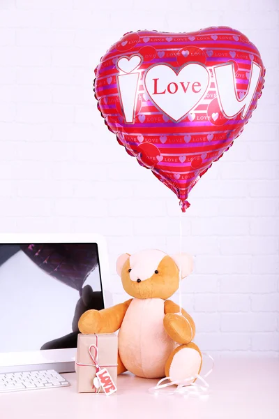 Teddybeer met huidige doos en liefde hart ballon op houten computer tafel, op de bakstenen muur achtergrond — Stockfoto