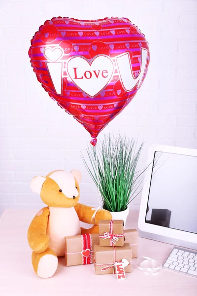 Teddy bear with present boxes, plant and love heart balloon on wooden  computer table, on the brick wall background — Stock Photo, Image