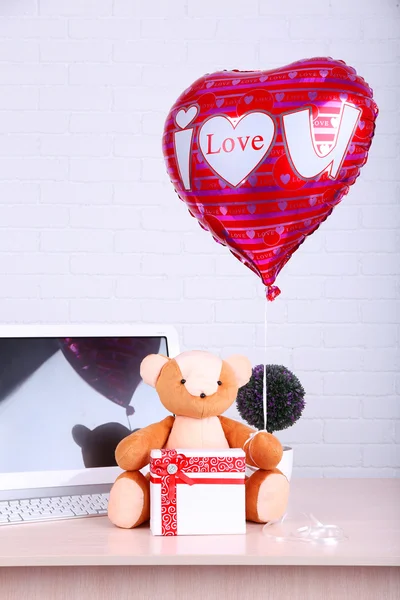 Urso de pelúcia com caixa presente, planta e amor balão de coração na mesa de computador de madeira, no fundo da parede de tijolo — Fotografia de Stock
