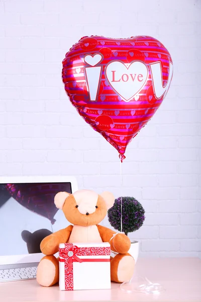 Teddy bear with present box, plant and love heart balloon on wooden  computer table, on the brick wall background — Stock Photo, Image