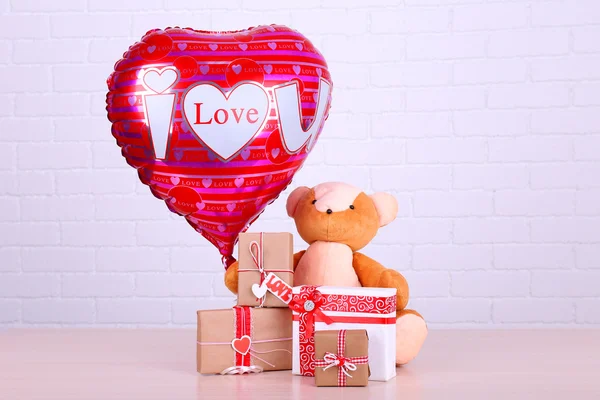 Teddy urso leva presentes e amor coração balão na mesa de madeira, no fundo da parede de tijolo — Fotografia de Stock