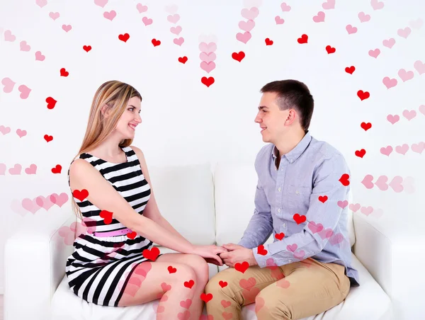 Loving couple sitting on sofa and heart-shaped frame, on light background — Stock Photo, Image