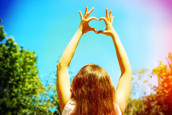 Молодая женщина держит руки в форме сердца обрамляясь на фоне неба — стоковое фото