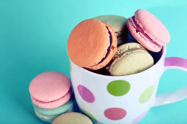 Assortment of gentle colorful macaroons in mug on color background — Stock Photo, Image