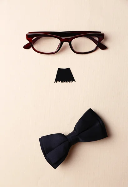 Glasses, mustache and bow tie forming man face on beige background — Stock Photo, Image