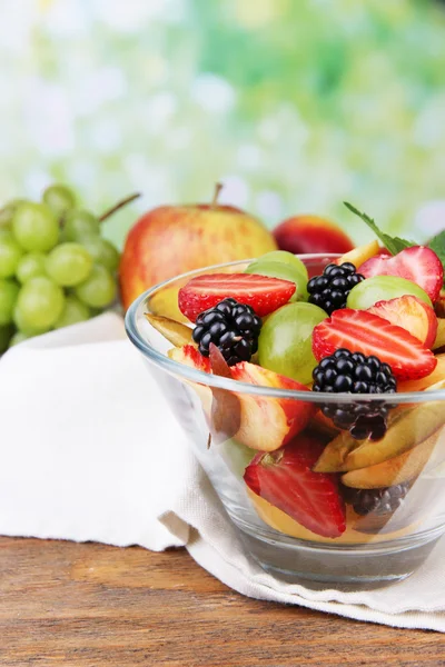 Fresh tasty fruit salad on wooden table, on nature background — Stock Photo, Image