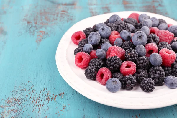 Geeiste Beeren auf Teller, auf farbigem Holzhintergrund — Stockfoto