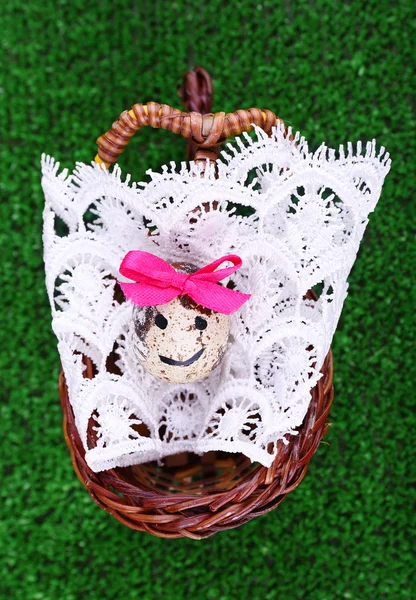 Single egg on lace napkin in wicker basket on green background — Stock Photo, Image