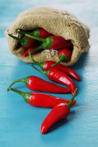 Red hot chili peppers in sack on wooden background — Stock Photo, Image