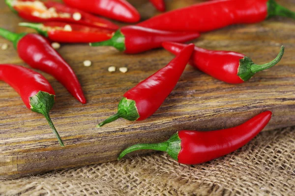 Rode hete chilipepertjes op houten bord, op zak achtergrond — Stockfoto