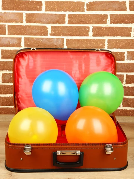 Stapel van ballonnen van verschillende kleuren in oude koffer, op bakstenen muur achtergrond — Stockfoto