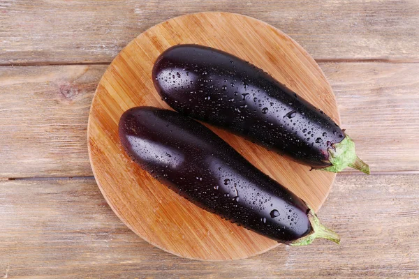 Aubergines on round cutting board on wooden background — Stock Photo, Image