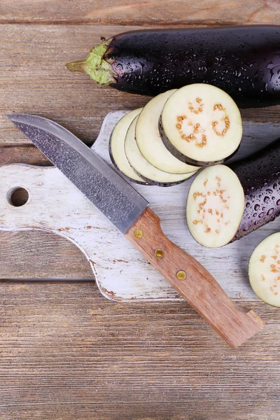 Chopped aubergines and knife on cutting board on wooden background — Stock Photo, Image