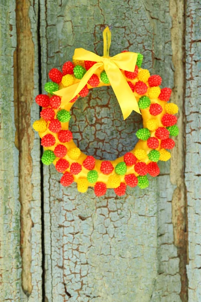 Beautiful wreath of candies hanging on old wooden door — Stock Photo, Image