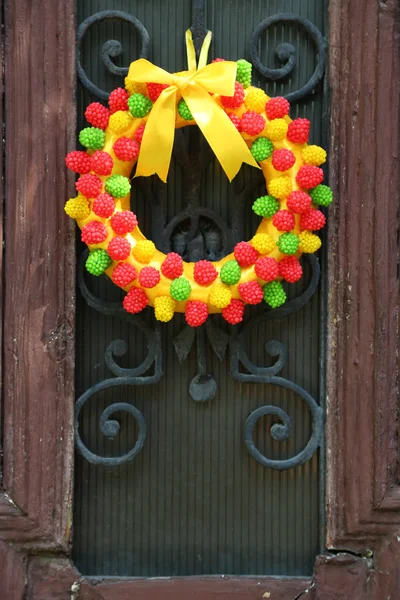 Beautiful wreath of candies hanging on old wooden door — Stock Photo, Image