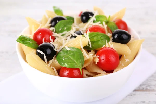 Pasta con pomodori, olive e foglie di basilico in ciotola su tovagliolo su fondo di legno — Foto Stock