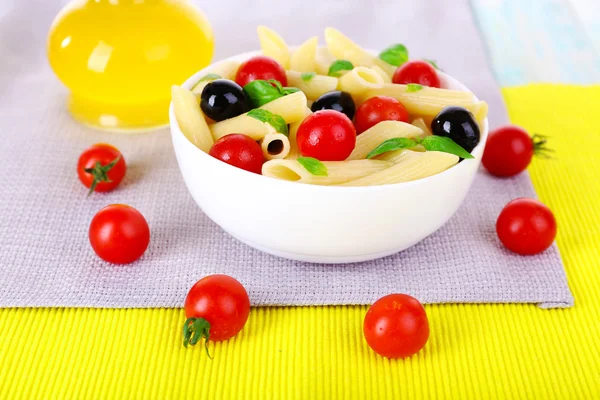 Pasta med tomater, oliven, olivenolie og basilikumblade i skål på serviet - Stock-foto