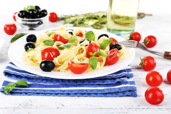 Spaghetti met tomaten, olijven en basilicum bladeren op plaat op servet op houten achtergrond — Stockfoto